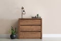 Wooden chest of drawers with houseplants and lamp near wall in room Royalty Free Stock Photo