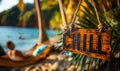 Wooden CHILL sign hanging on a hammock between palm trees on a tropical beach with a serene ocean view, epitomizing