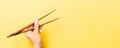 Wooden chopsticks in female hand on yellow background with empty space for your idea. Tasty food concept Royalty Free Stock Photo