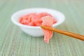 Chopsticks hold a piece of pink marinated ginger on a background of a white porcelain bowl over a green wicker table mat. Royalty Free Stock Photo