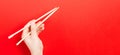 Wooden chopsticks in male hand on red background with empty space for your idea. Tasty food concept Royalty Free Stock Photo