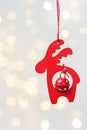 Wooden Christmas ornament red deer with bell hanging on white background with golden garland bokeh lights. Magic holiday Royalty Free Stock Photo