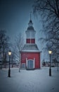 Wooden church in Jukkasjarvi, dry leafless trees, and two lit street lights in winter