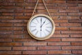 Wooden wall clock with roman numerals hanging in a red brick wall. Royalty Free Stock Photo