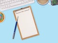 Wooden clipboard with blank paper and pen, keyboard, cactus coffee cup on blue work table. Top view with space for text. Royalty Free Stock Photo