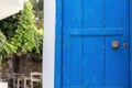Wooden closed blue old door with rusty handle and keyhole. Greek island blur cafe, plant background Royalty Free Stock Photo