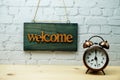 Welcome sign and alarm clock with space copy on white brick wall background Royalty Free Stock Photo