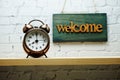 Welcome sign and alarm clock with space copy on white brick wall background Royalty Free Stock Photo