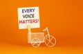 Wooden clothespin with white sheet of paper. Text `every voice matters`. Miniature bicycle model. Beautiful orange background.