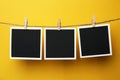 Wooden clothespins with empty instant frames on twine against yellow background. Space for text Royalty Free Stock Photo