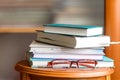 On a wooden console in the room, a stack of books for reading with female glasses for vision.