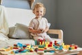 Wooden construction set. Montessori learning approach. Cognitive development puzzles. Happy smiling little blonde baby girl