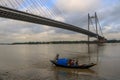 Wooden country boat ride on the river Ganges on a cloudy day with the Vidyasagar Setu (bridge) at the backdrop.