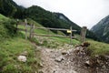 Wooden cow gate with passage for hikers, in the mountains, gravel path, fir forest with fog in the background, during the day Royalty Free Stock Photo