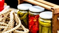 Wooden crate with glass jars with pickled red bell peppers and pickled cucumbers (pickles) isolated.