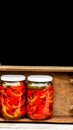 Wooden crate with glass jars with pickled red bell peppers.Preserved food concept, canned vegetables isolated in a rustic