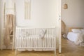 Wooden crib with cushions standing in real photo of white kid room interior with blanket on ladder