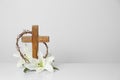 Wooden cross, crown of thorns and blossom lilies on table against light background