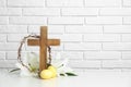 Wooden cross, crown of thorns, Easter eggs and blossom lilies on table against brick wall Royalty Free Stock Photo