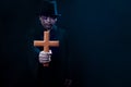 Wooden cross in hand of man in spooky black costume standing in dark background, sorcerer wizard holding wood cross going to