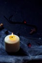 Halloween wooden cross lying next to a burning candle on a web with spiders and bats on a black background. vertical