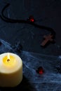 Halloween wooden cross lying next to a burning candle on a web with spiders and bats on a black background. vertical