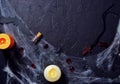 Halloween wooden cross lying next to a burning candle on a web with spiders and bats on a black background. horizontal, flat lay,