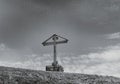 Wooden cross stands on a hill on a background of sky. Black and white photo.