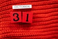 Wooden cube calendar showing October 31, Halloween isolated on red background red knitted sweater