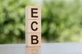 Wooden cubes with acronym ECB arranged in a vertical pyramid, on the green nature background. ECB short for European Central Bank