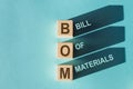 Wooden cubes building the word BOM bill of materials on blue background Royalty Free Stock Photo