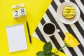 Wooden cubes calendar April 28th. Cup of coffee, yellow donut and rose on black and white napkin, empty open notepad for text on