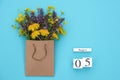 Wooden cubes calendar August 5 and field colorful rustic flowers in craft package on blue background. Greeting card Flat Lay