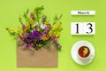 Wooden cubes calendar March 13. Cup of herbs tea, kraft envelope with multi colored flowers on green background. Concept hello