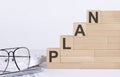 Wooden cubes with letters PLAN on the white table with keyboard and glasses