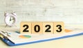 Wooden cubes lie on a folder with financial charts on a gray background. The cubes make up the word 2023.