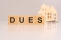 wooden cubes on a table with text DUES, model house and keys on background. concept of business, financial, investment