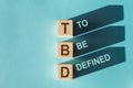 Wooden cubes with TBD meaning To Be Defined cast long shadows on a blue surface Royalty Free Stock Photo