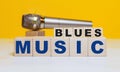 Wooden cubes with the word BLUES MUSIC on a yellow background and a concert microphone. Musical concept