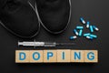 Wooden cubes with word Doping, sport shoes and drugs on black background, flat lay