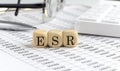 Wooden cubes with the word ESR - Erythrocyte Sedimentation Rate on a financial background with chart, calculator, pen and glasses