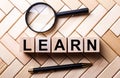 Wooden cubes with the word LEARN stand on a wooden background between a magnifying glass and a pen