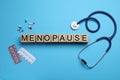 Wooden cubes with word Menopause, stethoscope and pills on light blue background, flat lay