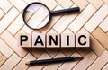 Wooden cubes with the word PANIC stand on a wooden background between a magnifying glass and a handle Royalty Free Stock Photo