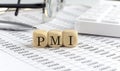 wooden cubes with the word PMI on a financial background with chart, calculator, pen and glasses, business concept Royalty Free Stock Photo