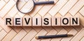 Wooden cubes with the word REVISION stand on a wooden background between a magnifying glass and a pen Royalty Free Stock Photo