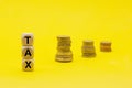 Wooden cubes with the word Tax on money climbing staits  pile of coins on yellow background  Tax Concept Royalty Free Stock Photo