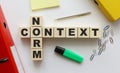 Wooden cubes with words NORM CONTEXT on the office desk. Folder and other office supplies