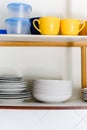 Wooden cupboard with piles of ceramic plates, cups and plastic containers Royalty Free Stock Photo