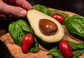 A wooden cutting board on a black background with an avocado in the center. All around, intense green basil leaves and bright red Royalty Free Stock Photo